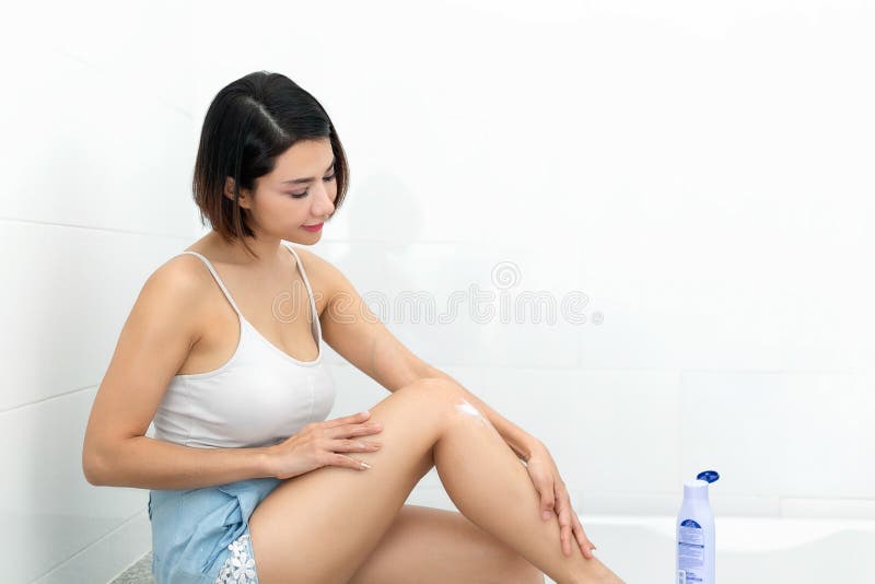 Mujer joven que aplica la loción del cuerpo en sus piernas fotografía de archivo Mujer joven que aplica la loción del cuerpo en sus piernas fotografía de archivo