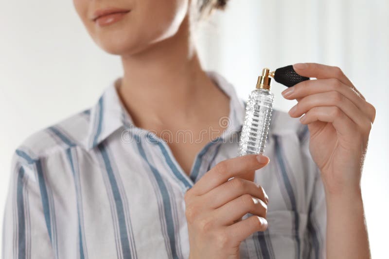 Mujer joven que aplica perfume en cuello contra fondo borroso foto de archivo Mujer joven que aplica perfume en cuello contra fondo borroso foto de archivo