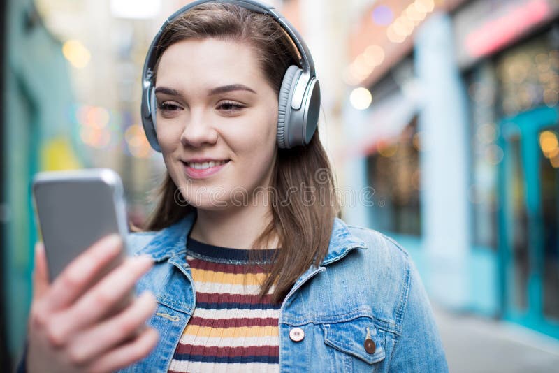 Mujer joven que camina a lo largo de la calle que fluye música de Pho móvil foto de archivo Mujer joven que camina a lo largo de la calle que fluye música de Pho móvil foto de archivo