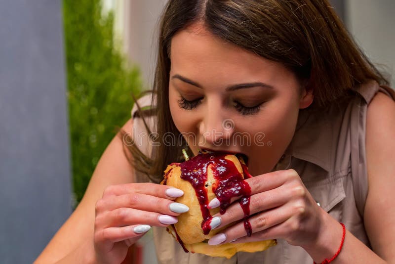 Mujer joven que come la hamburguesa en restaurante Cierre encima de la cara y de las manos cubiertas en salsa imágenes de archivo libres de regalías Mujer joven que come la hamburguesa en restaurante Cierre encima de la cara y de las manos cubiertas en salsa imágenes de archivo libres de regalías