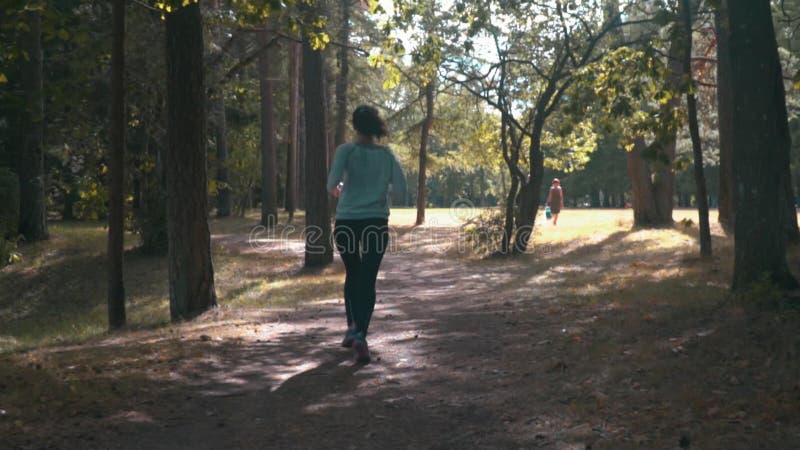 Mujer joven que corre en el bosque en la tarde soleada del verano