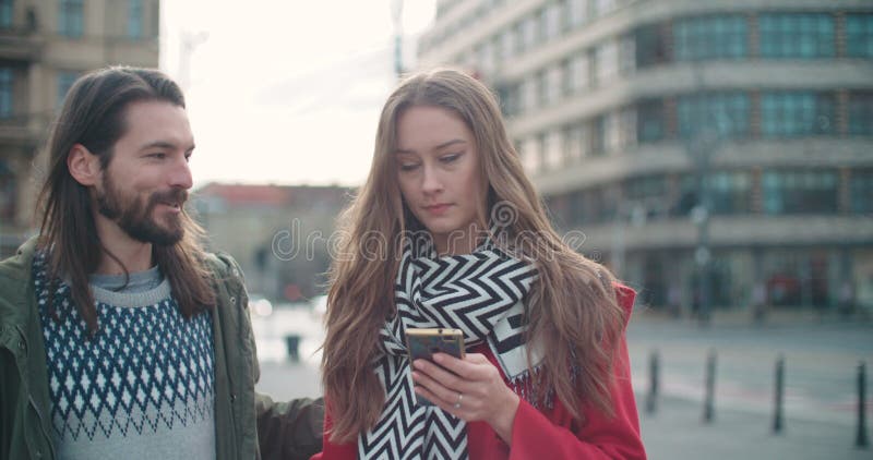 Mujer joven que espera a su novio y que mecanografía en el teléfono