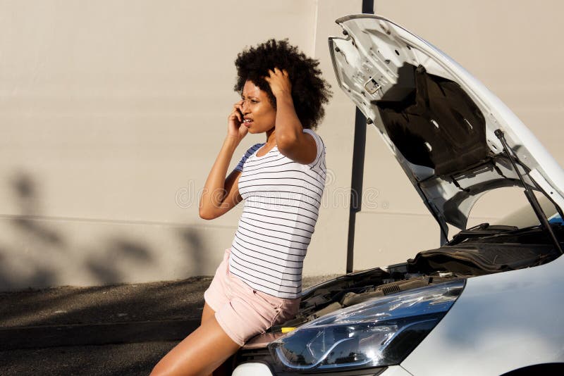 Mujer joven que hace una pausa el coche analizado y que hace la llamada de teléfono para la ayuda