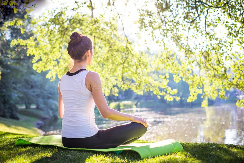Mujer joven que hace yoga en parque de la mañana cerca del lago foto de archivo libre de regalías Mujer joven que hace yoga en parque de la mañana cerca del lago foto de archivo libre de regalías