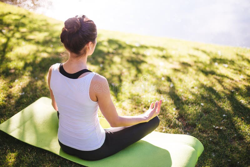 Mujer joven que hace yoga en parque de la mañana cerca del lago fotografía de archivo Mujer joven que hace yoga en parque de la mañana cerca del lago fotografía de archivo