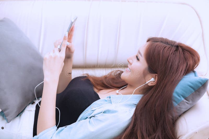 Mujer joven que juega el teléfono elegante que miente en sofá fotografía de archivo Mujer joven que juega el teléfono elegante que miente en sofá fotografía de archivo