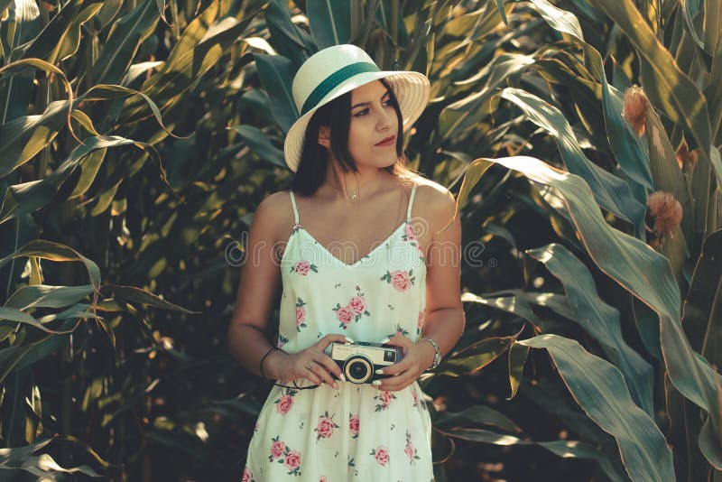 Mujer joven que lleva un vestido blanco florido que toma las fotos con la cámara retra de la foto imagenes de archivo Mujer joven que lleva un vestido blanco florido que toma las fotos con la cámara retra de la foto imagenes de archivo