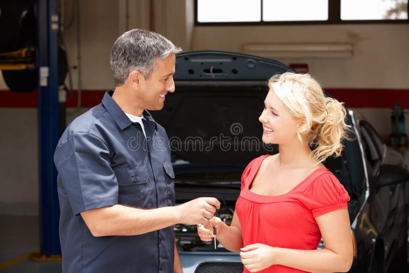 Mujer joven que recoge el coche del taller de reparaciones fotos de archivo libres de regalías Mujer joven que recoge el coche del taller de reparaciones fotos de archivo libres de regalías