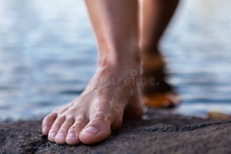 Mujer joven que sale de los pies desnudos del agua en una roca fotografía de archivo Mujer joven que sale de los pies desnudos del agua en una roca fotografía de archivo