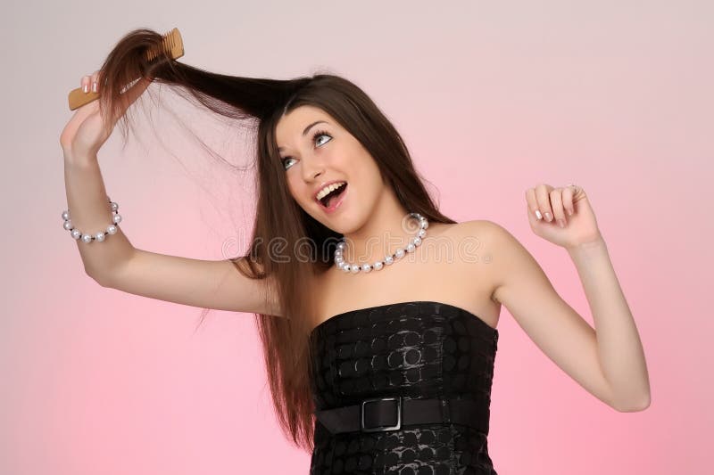 Young woman combing her hair. pink-gray background. Young woman combing her hair. pink-gray background