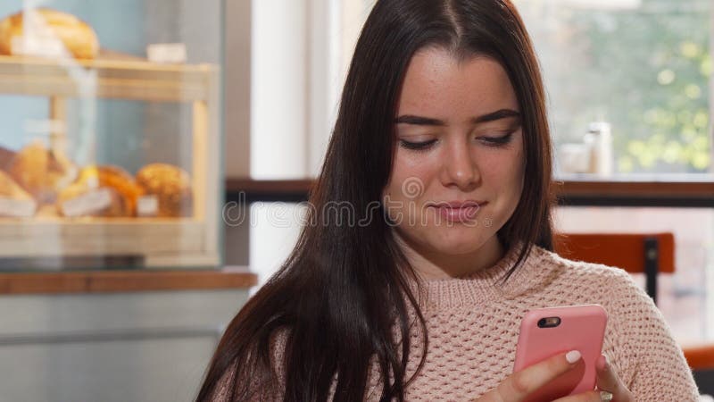 Mujer joven que sonríe, usando su teléfono elegante en la cafetería fotografía de archivo libre de regalías Mujer joven que sonríe, usando su teléfono elegante en la cafetería fotografía de archivo libre de regalías