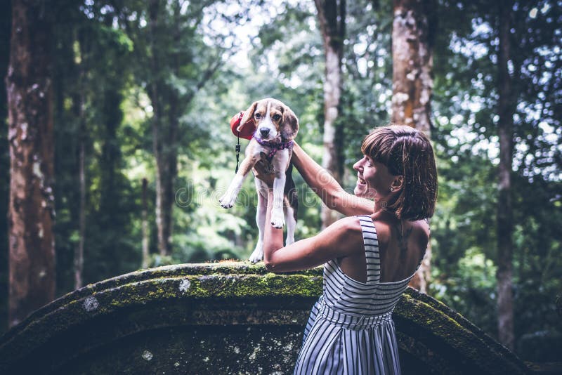 Mujer joven que sostiene su perro del beagle del perrito en naturaleza de la isla tropical de Bali, Indonesia fotos de archivo libres de regalías Mujer joven que sostiene su perro del beagle del perrito en naturaleza de la isla tropical de Bali, Indonesia fotos de archivo libres de regalías