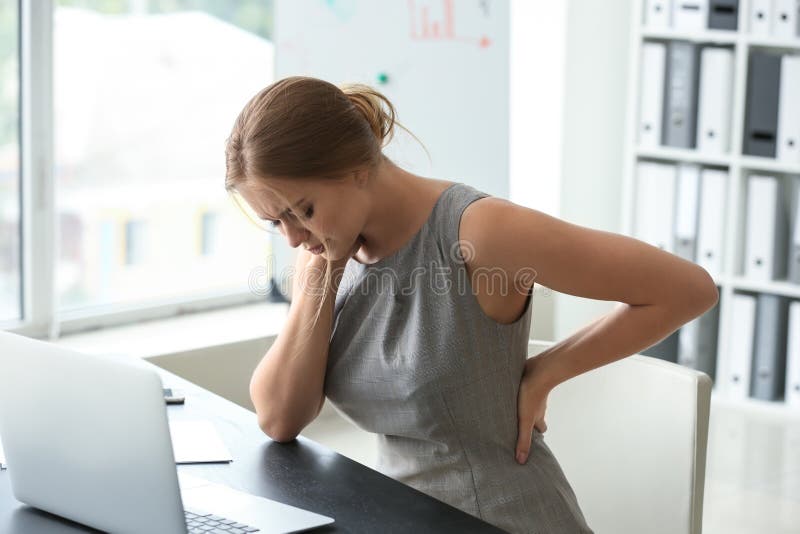 Mujer joven que sufre de dolor de espalda en oficina fotos de archivo Mujer joven que sufre de dolor de espalda en oficina fotos de archivo