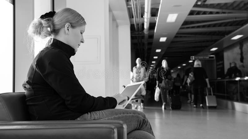 Mujer joven que usa su PC digital de la tableta en un salón del aeropuerto imagen de archivo Mujer joven que usa su PC digital de la tableta en un salón del aeropuerto imagen de archivo