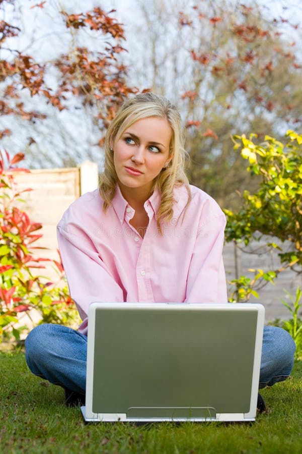 Mujer joven reflexiva usa computadora portátil en su jardín en casa imagenes de archivo Mujer joven reflexiva usa computadora portátil en su jardín en casa imagenes de archivo