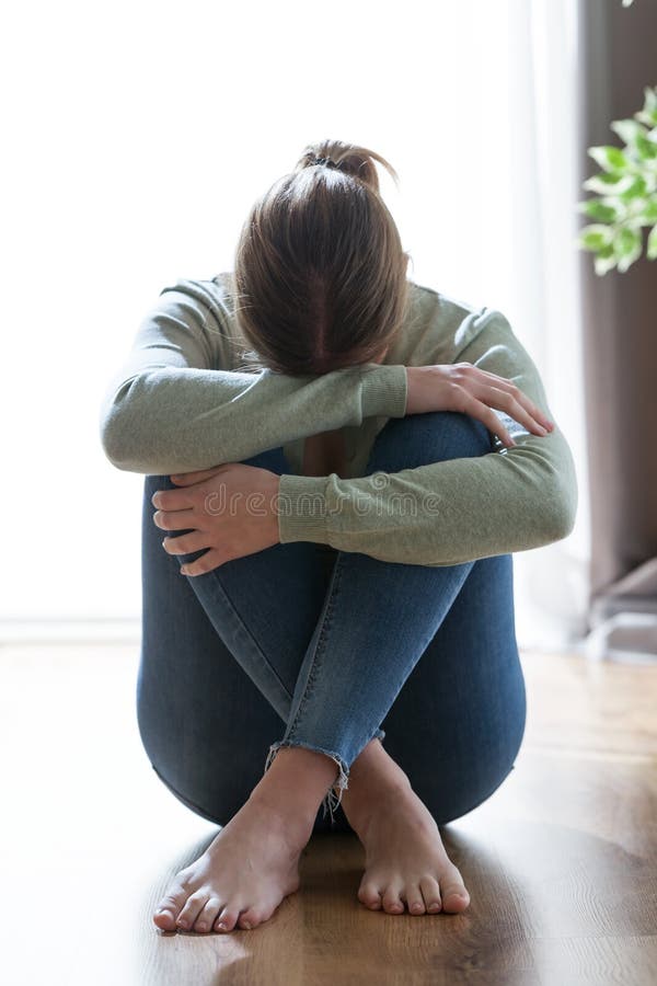 Mujer joven sola y deprimida infeliz que oculta su cara entre las piernas en casa imagenes de archivo Mujer joven sola y deprimida infeliz que oculta su cara entre las piernas en casa imagenes de archivo