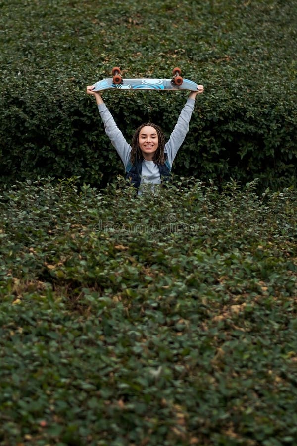 Mujer joven sonriente que salta entre los arbustos verdes fotografía de archivo Mujer joven sonriente que salta entre los arbustos verdes fotografía de archivo