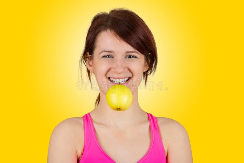 Mujer joven sonriente que sostiene la manzana verde en sus dientes imágenes de archivo libres de regalías Mujer joven sonriente que sostiene la manzana verde en sus dientes imágenes de archivo libres de regalías