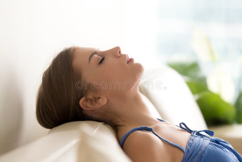 Mujer joven tranquila que se relaja en el sofá acogedor, aire fresco de respiración imagen de archivo Mujer joven tranquila que se relaja en el sofá acogedor, aire fresco de respiración imagen de archivo