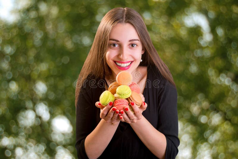 Mujer joven y sonriente que sostiene un manojo de macarrones coloridos encendido fotografía de archivo libre de regalías Mujer joven y sonriente que sostiene un manojo de macarrones coloridos encendido fotografía de archivo libre de regalías