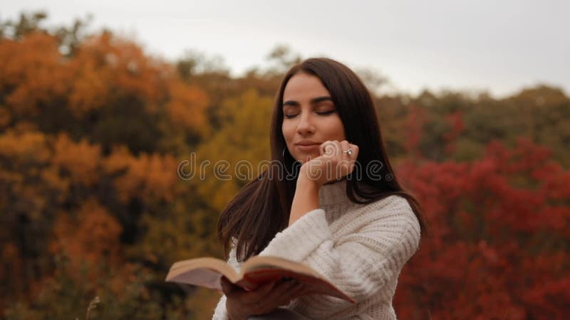 Mujer leyendo un libro sentado en el bosque de otoño inclinándose cabeza a mano