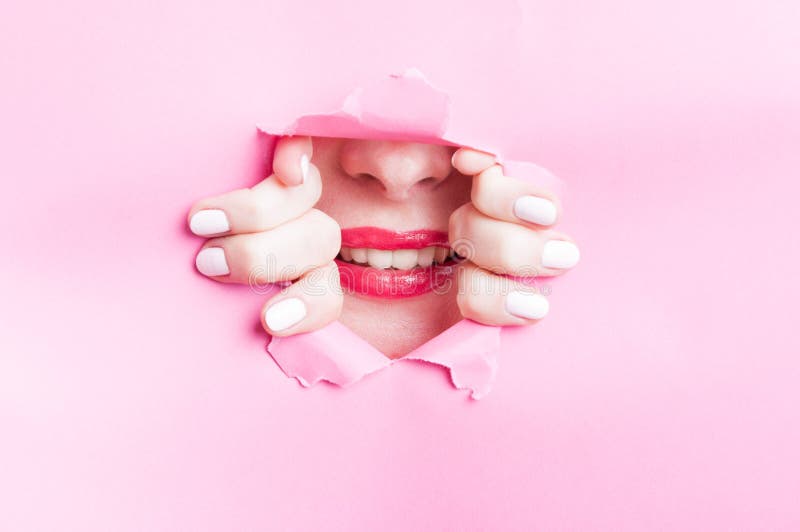 Mujer linda que muestra sonrisa hermosa a través de la cartulina rosada rasgada foto de archivo Mujer linda que muestra sonrisa hermosa a través de la cartulina rosada rasgada foto de archivo