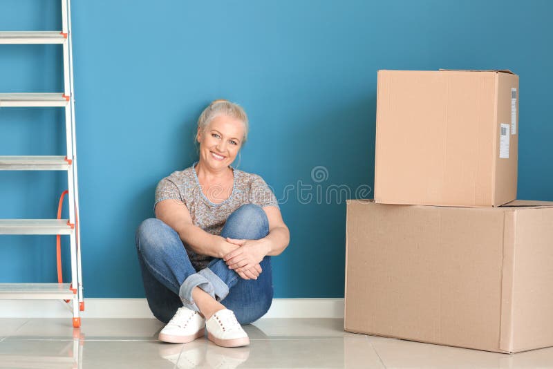Mujer madura con las cajas móviles que se sientan en piso en el nuevo hogar fotos de archivo Mujer madura con las cajas móviles que se sientan en piso en el nuevo hogar fotos de archivo