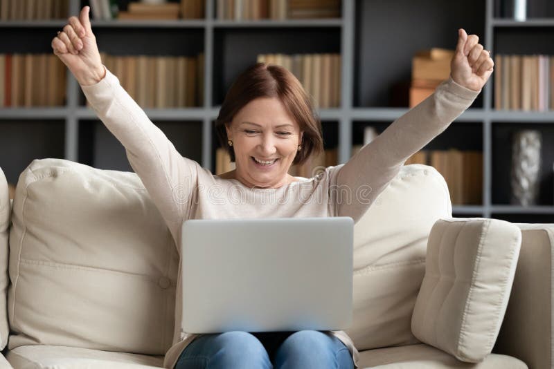 Mujer madura emocionada mirando la pantalla del portátil leyendo buenas noticias