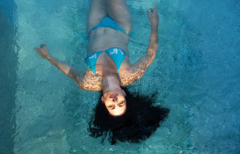 Mujer madura hermosa en la mejor edad con el pelo rizado oscuro en bikini azul en la luz del sol del sol que flota ingrávido imágenes de archivo libres de regalías Mujer madura hermosa en la mejor edad con el pelo rizado oscuro en bikini azul en la luz del sol del sol que flota ingrávido imágenes de archivo libres de regalías