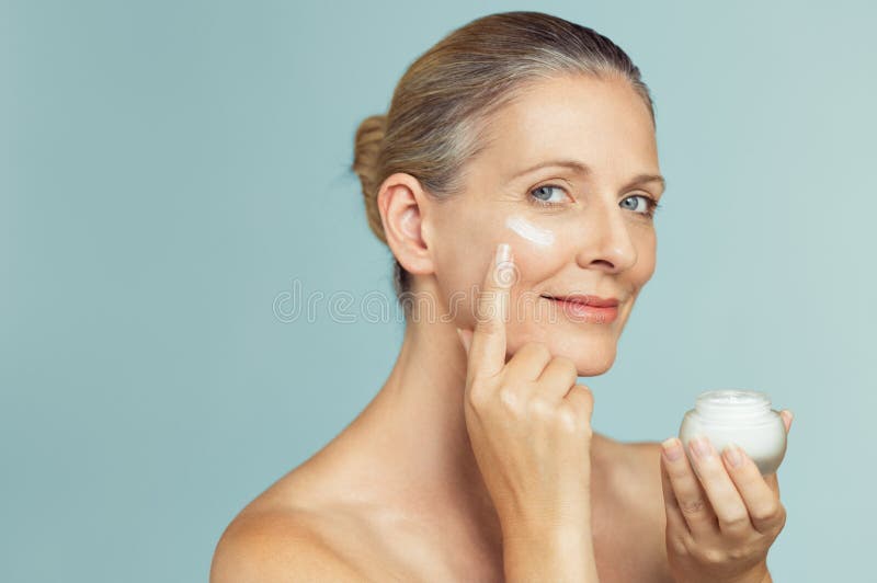 Mujer madura que aplica la crema de piel en cara