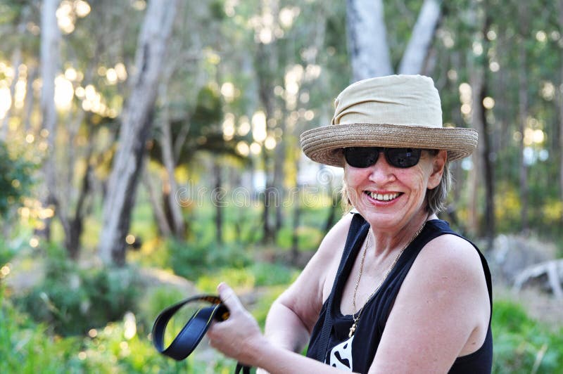 Mujer madura sonriente feliz en sombrero en caminar del rastro del bosque foto de archivo libre de regalías Mujer madura sonriente feliz en sombrero en caminar del rastro del bosque foto de archivo libre de regalías