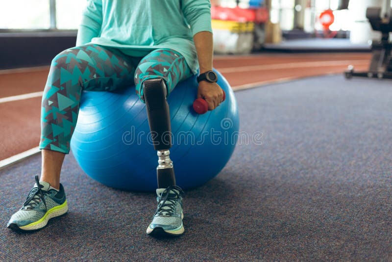 Mujer mayor activa discapacitada que ejercita con pesa de gimnasia mientras que se sienta en bola del ejercicio imagen de archivo Mujer mayor activa discapacitada que ejercita con pesa de gimnasia mientras que se sienta en bola del ejercicio imagen de archivo