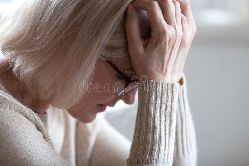 Mujer mayor cansada triste que se sostiene principal en las manos que sienten dolor de cabeza