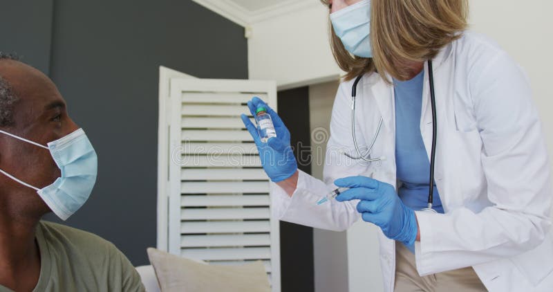 Mujer mayor caucásica doctor con máscara facial preparar vacuna para hombre afroamericano metrajes