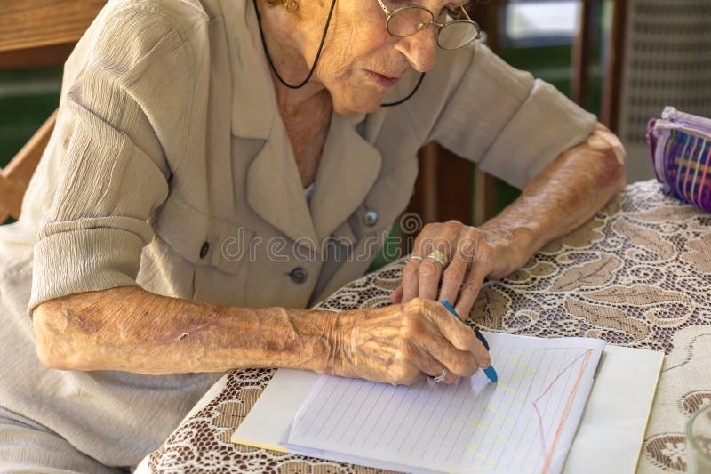 Mujer mayor dibujando líneas coloridas en un cuaderno con lápices de cera fotografía de archivo libre de regalías