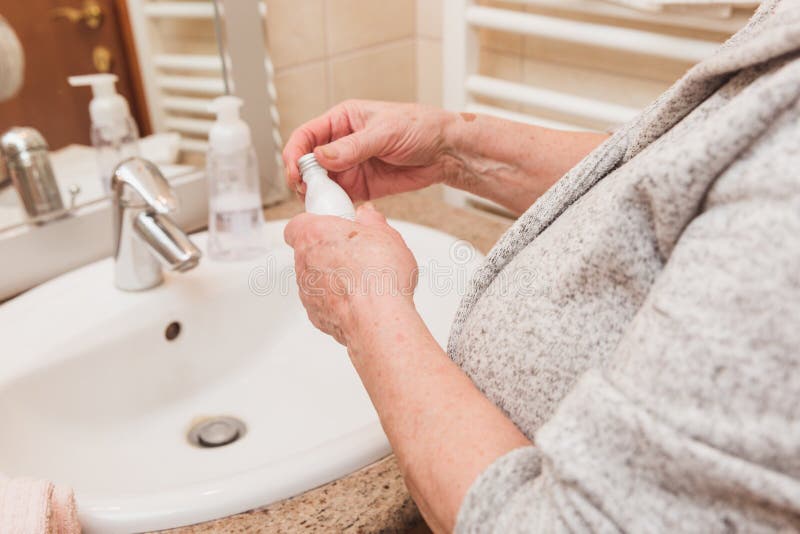 Mujer mayor en la albornoz que aplica la crema de la mano en el cuarto de baño, primer imagen de archivo Mujer mayor en la albornoz que aplica la crema de la mano en el cuarto de baño, primer imagen de archivo