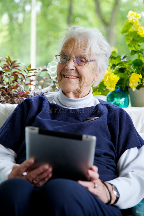Mujer mayor feliz que usa una tableta que mira la cámara y la risa imagen de archivo libre de regalías Mujer mayor feliz que usa una tableta que mira la cámara y la risa imagen de archivo libre de regalías