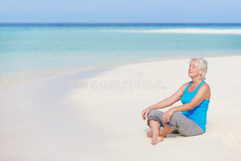 Mujer mayor Meditating en la playa hermosa imagen de archivo Mujer mayor Meditating en la playa hermosa imagen de archivo