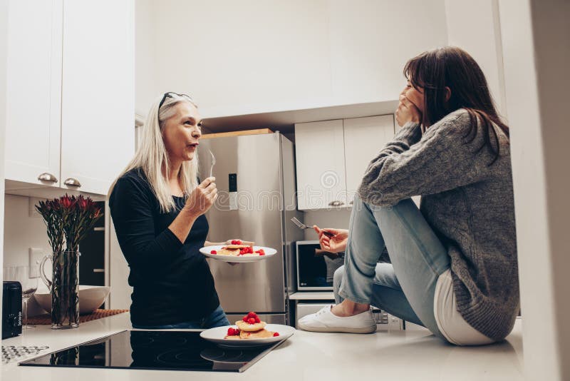 Mujer mayor que come las galletas de una situación de la placa en la cocina que habla con una mujer Dos mujeres que hablan mientr fotos de archivo libres de regalías Mujer mayor que come las galletas de una situación de la placa en la cocina que habla con una mujer Dos mujeres que hablan mientr fotos de archivo libres de regalías
