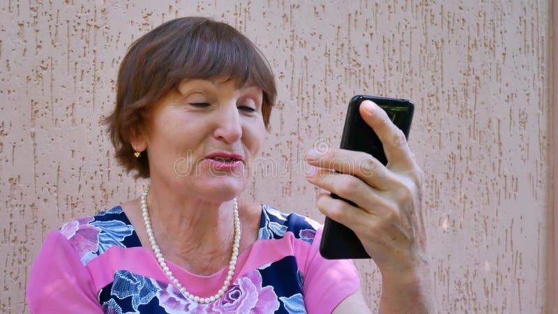 Mujer mayor que tiene charla video en línea usando smartphone negro