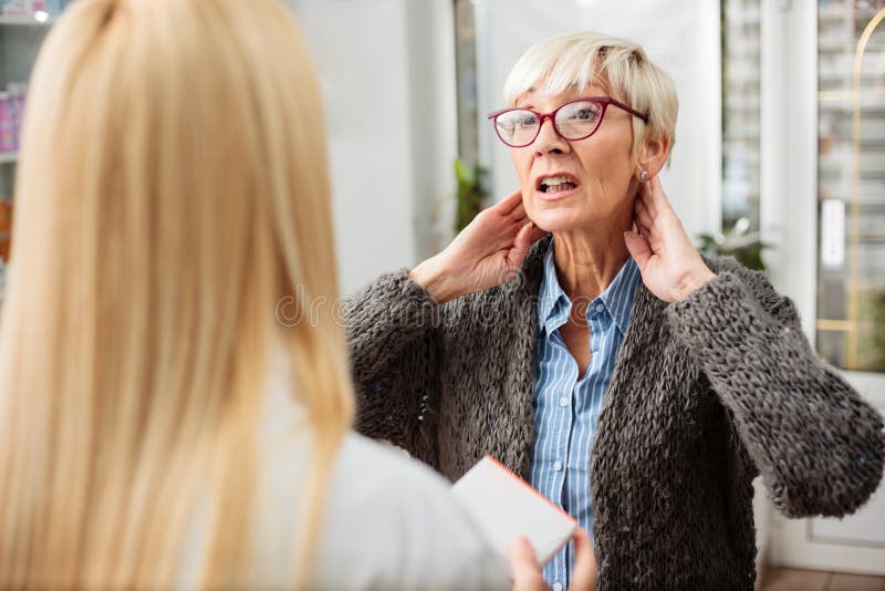Mujer mayor seria con problemas del dolor o de la tiroides de cuello que consulta con el doctor foto de archivo Mujer mayor seria con problemas del dolor o de la tiroides de cuello que consulta con el doctor foto de archivo