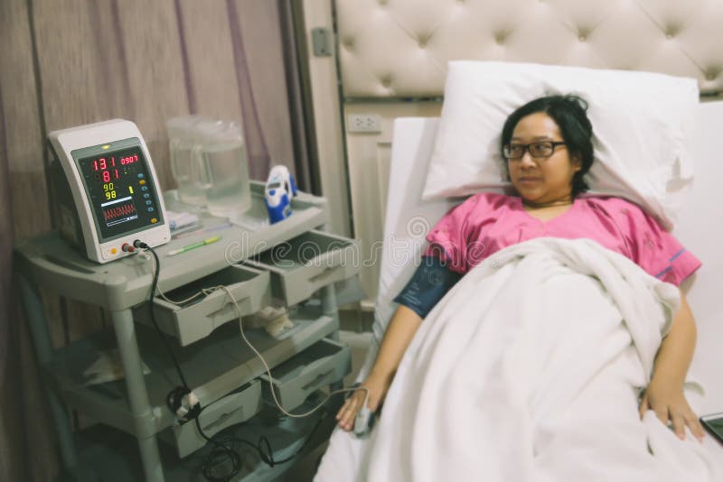 Mujer mientras que miente en una cama de hospital con un equipamiento médico del ritmo cardíaco fotografía de archivo Mujer mientras que miente en una cama de hospital con un equipamiento médico del ritmo cardíaco fotografía de archivo