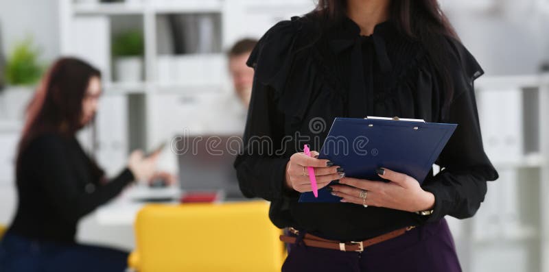 Brunette women hold in arms pink pen and paper clipped to pad closeup colleagues in background. White collar worker at workspace officer highly pay smart serious headhunter offer. Brunette women hold in arms pink pen and paper clipped to pad closeup colleagues in background. White collar worker at workspace officer highly pay smart serious headhunter offer