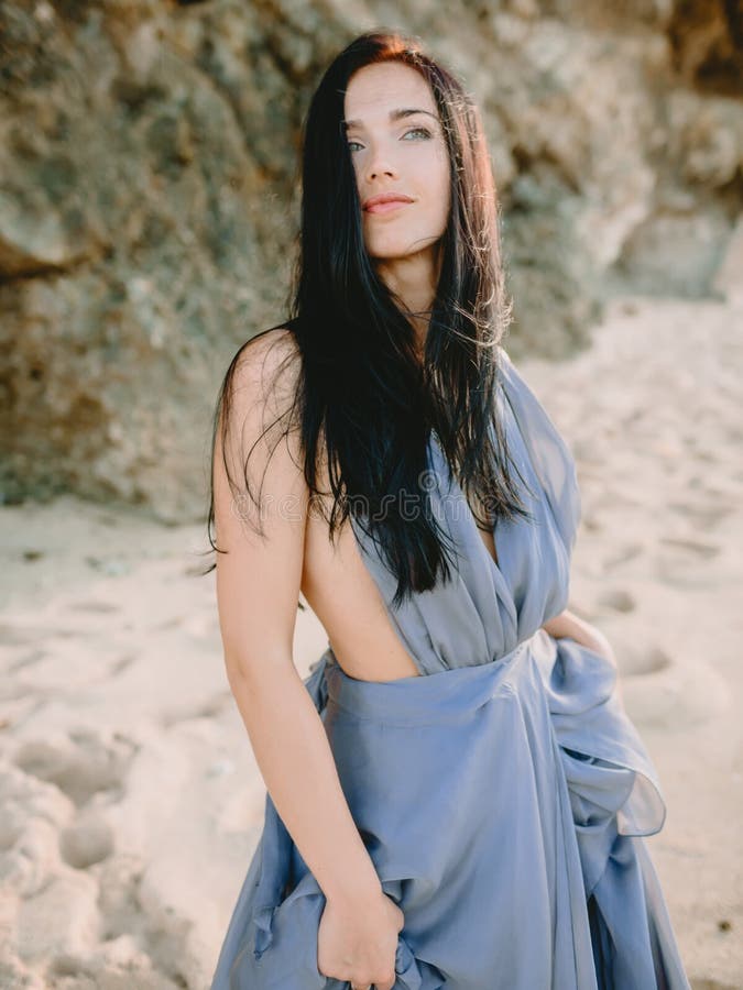 Mujer Morena Que Presenta En Vestido Azul Elegante En Playa En Los Colores  De La Puesta Del Sol O De La Salida Del Sol Mujer De L Imagen de archivo -  Imagen