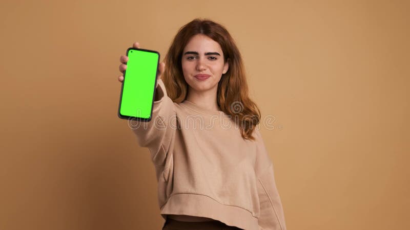 Mujer mostrando el celular con pantalla verde en el estudio almacen de video