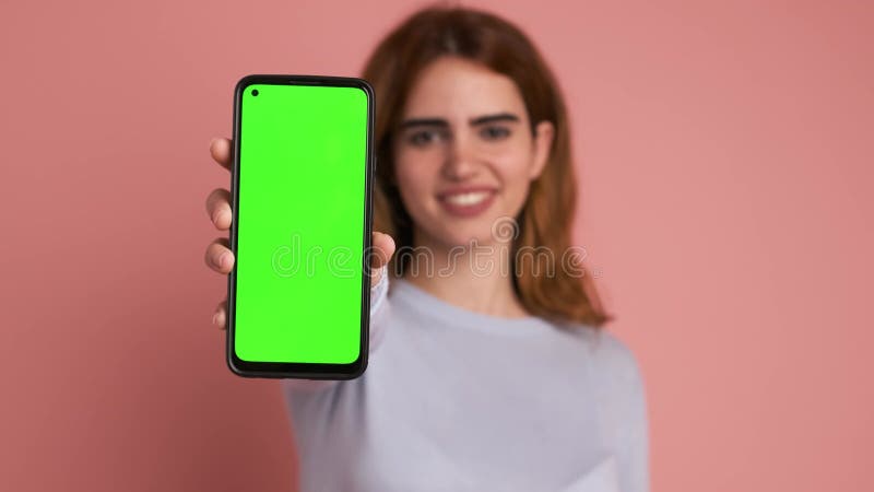 Mujer mostrando el celular con pantalla verde en el estudio almacen de video