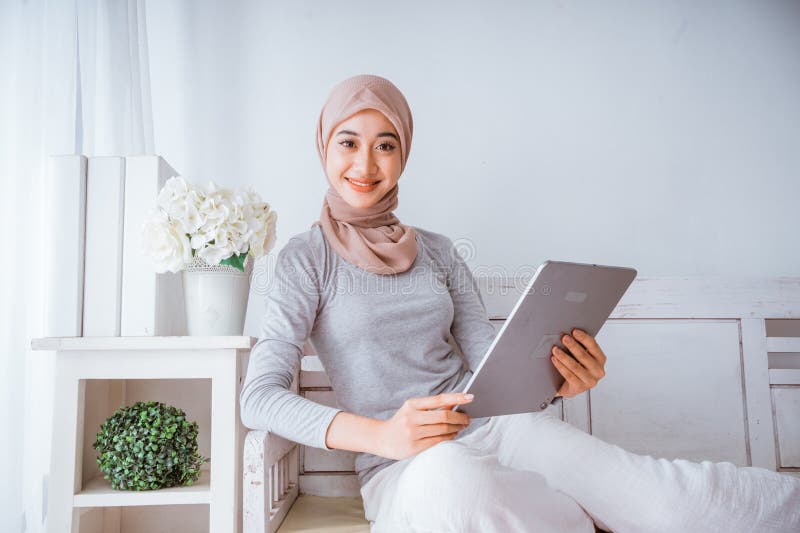Mujer musulmana hijab mirando a su casa hace el tutorial desde tablet imagen de archivo