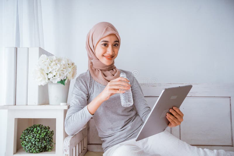 Mujer musulmana hijab mirando a su casa hace el tutorial desde tablet. Mujer musulmana hijab mirando a casa hace el tutorial de un tablet en un colchón de una habitación felizmente