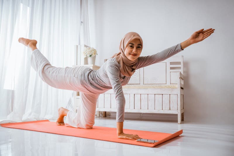 Mujer musulmana hijab sonriendo calentándose antes de hacer ejercicio haciendo posadas de yoga fotografía de archivo libre de regalías