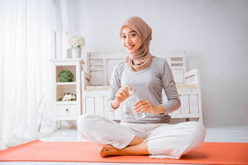 Mujer musulmana hijab sonríe bebiendo de una botella después de hacer ejercicio en casa de yoga fotos de archivo libres de regalías